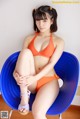 A woman in an orange bikini sitting on a blue chair.